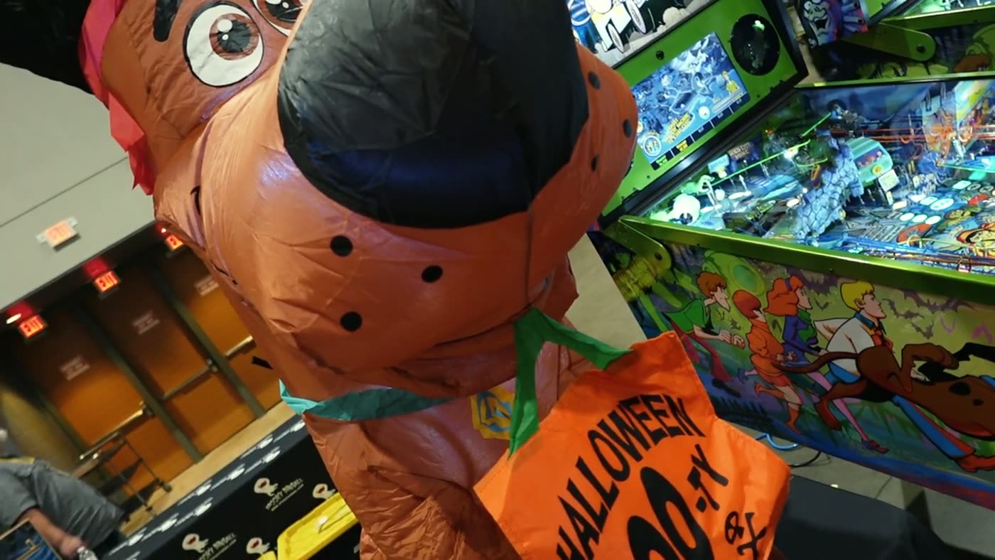 Persona disfrazada junto a una máquina de pinball de Scooby-Doo